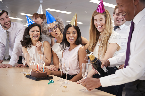 Colleagues celebrating a birthday in office pour champagne Stock Photo by monkeybusiness