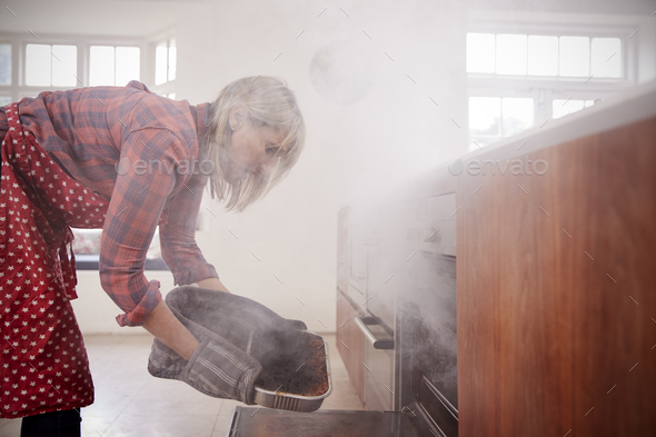 Middle aged woman opening smoke filled oven in the kitchen