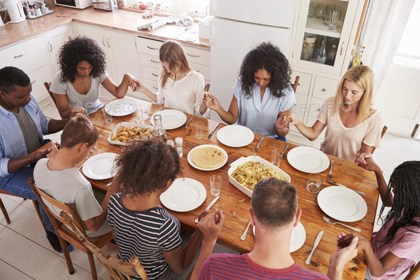 Two Families Saying Grace Before Eating Meal Together Stock Photo by monkeybusiness