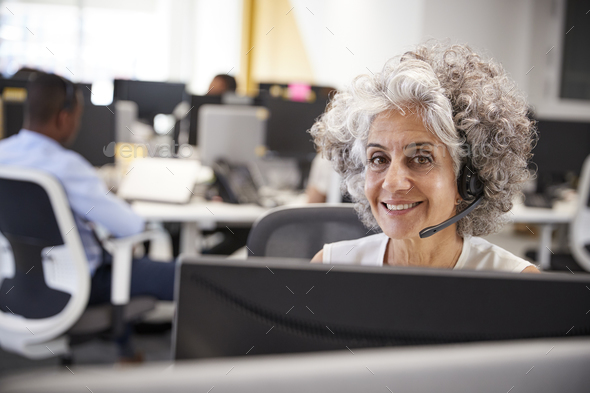 Middle aged woman working at computer with headset in office Stock Photo by monkeybusiness
