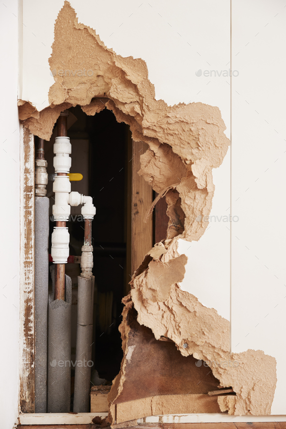 Damaged wall exposing burst water pipes after flood, vertical Stock Photo by monkeybusiness