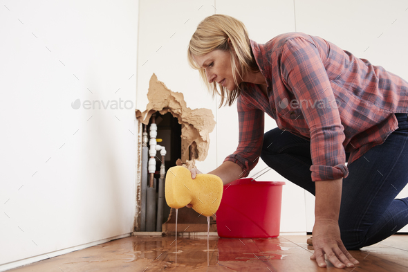 Worried woman mopping up water from a burst pipe with sponge Stock Photo by monkeybusiness