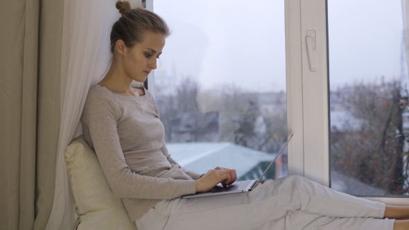 Beautiful Woman Typing on Her Laptop and Sitting on Windowsill