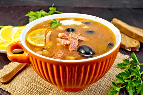 Solyanka with lemon and black olives in bowl on dark board - Stock Photo - Images
