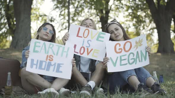 Three Young Hippies Showing Posters Earth Is Home Love Is Love Go Vegan Looking Camera alt