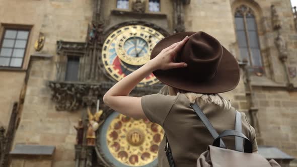woman in hat and backpack near famous clock in Prague, Czech Republic