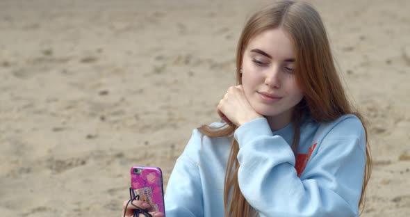 Beautiful Young Girl Sitting with A Mobile Phone on The Beach