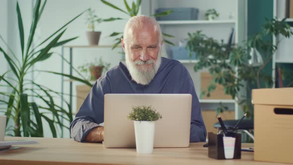 Concentrated Elderly Businessman Working Online While Sitting at His Desk alt