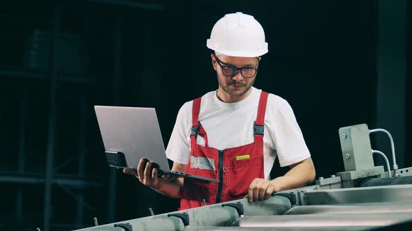Factory Worker with a Laptop Is Monitoring the Rolling Conveyor alt