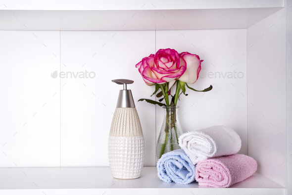 Stack of towels with a soap dispenser and roses in vasein a bathroom closeup - Stock Photo - Images