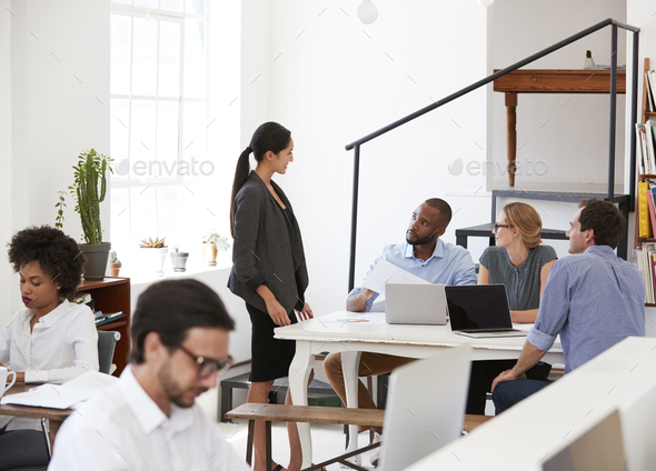 Woman talking with colleagues at a desk in open plan office Stock Photo by monkeybusiness