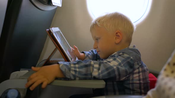 Little Boy Traveling in an Airplane Playing with a Tablet Computer