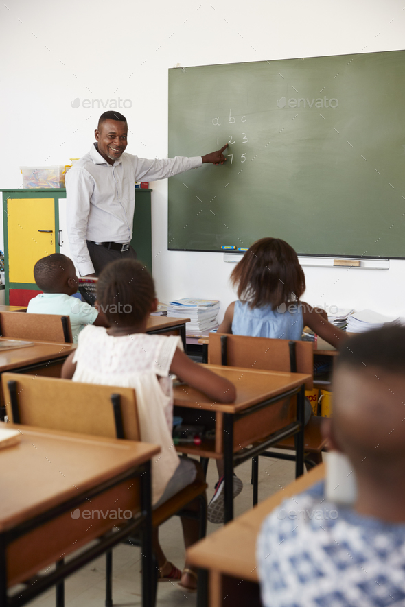 Teacher at chalkboard in elementary school class, vertical Stock Photo by monkeybusiness