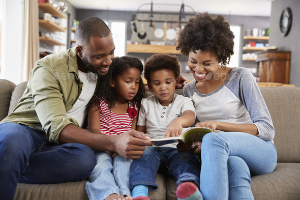 Family Sitting On Sofa In Lounge Reading Book Together Stock Photo by monkeybusiness