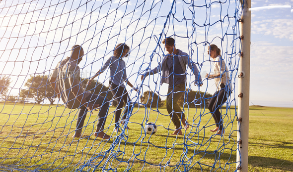 Two couples enjoy a game of football, seen through goal net Stock Photo by monkeybusiness