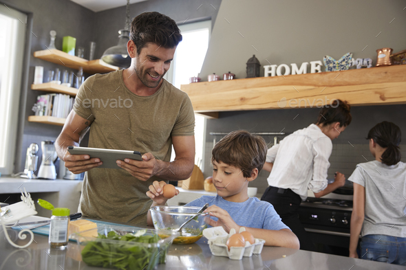 Family In Kitchen Following Recipe On Digital Tablet Together Stock Photo by monkeybusiness