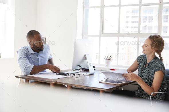 Young man and woman talking across their desks in an office Stock Photo ...