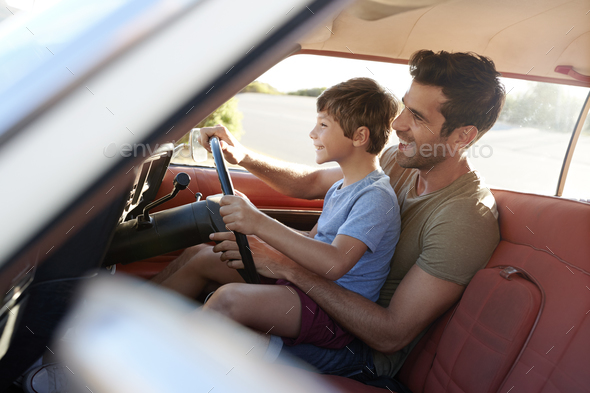 Father Teaching Young Son To Drive Car On Road Trip Stock Photo by monkeybusiness