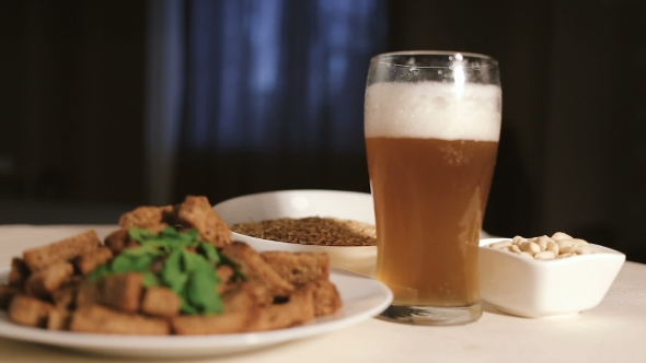 A Glass with Beer and Snacks on a Plate on a Dark Table.