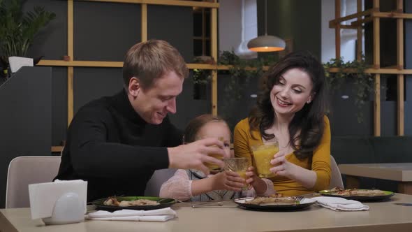 Positive Father Mother and Daughter Clinking Juice Glasses and Looking Away Smiling alt