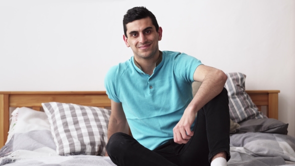 Happy Arabic Man Smiling, Sitting on Bed at Home