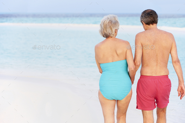 Rear View Of Senior Romantic Couple Walking In Tropical Sea Stock Photo by monkeybusiness