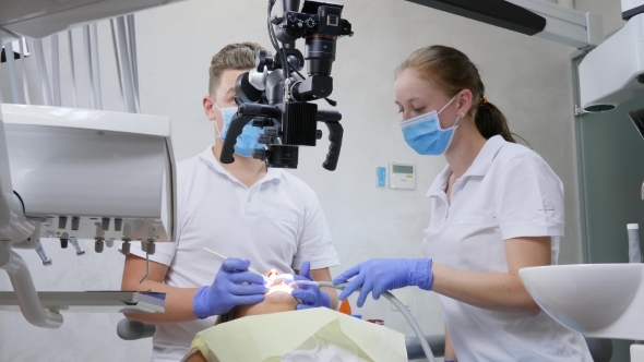 Specialist and Assistant Use Optical Microscope To Conduct an Operation in Mouth of Lying Patient in alt