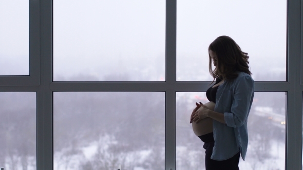 A Happy Pregnant Woman Stands at a Large Panoramic Window Located at a High Altitude He Touches His alt