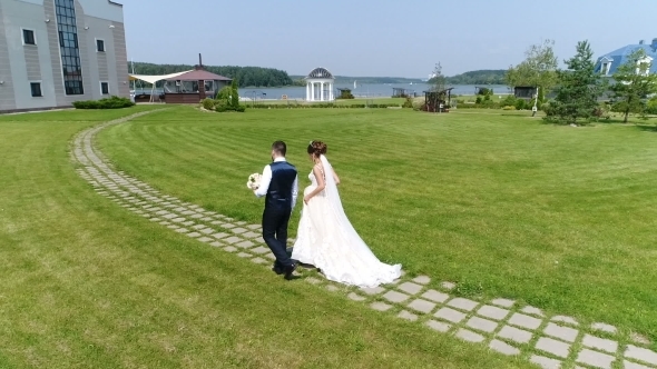 Groom and Bride Walking Along Green Grass