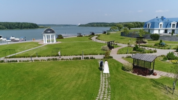 Groom and Bride Walking Along Green Grass