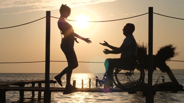 Silhouette of Disabled Man and Woman Against Sun, Romantic Meeting on Waterfront alt