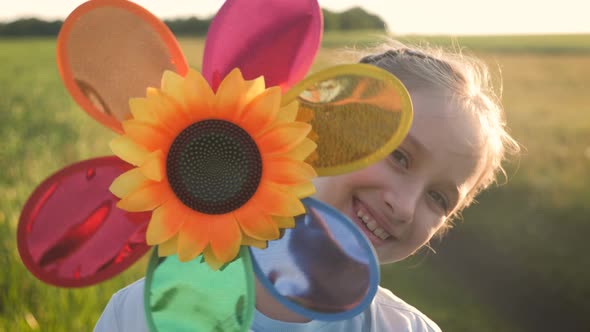 Happy Girl Holding Wind Toy in Green Field, Rejoicing Life. Cheerful Child in the Meadow with Wind alt