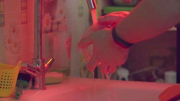 Hands of a Man Who Washes a Glass Mug The Water Tap, Red, Is Very Open