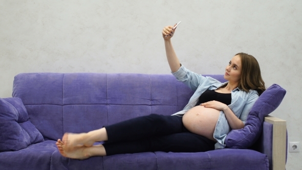 Beautiful Pregnant Woman Sitting on Sofa in Living Room Selfie for Social Networks alt