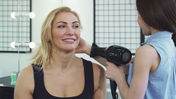 Gorgeous Woman Smiling while Her Daughter Blow Drying Her Hair alt