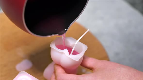 A woman occupied with hand made candles production, pouring melted wax into the mold. Slow motion alt