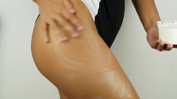 A woman with a perfect body applies a refreshing cream or body lotion to her leg.