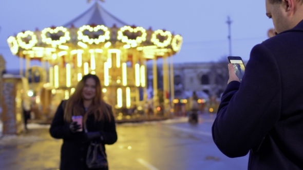 Husband Makes Photo of His Wife Using Phone on the Carousel Background alt