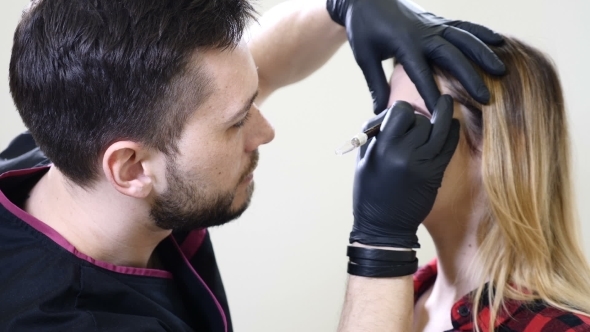 Male Beautician in Black Gloves Making Permanent Makeup Procedure on Female Eyebrows Beautician