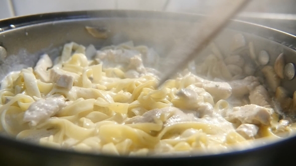 Macaroni and Mushrooms Are Fried on a Pan. A Wooden Spatula Mixes Them Slowly