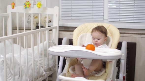 Baby with Tangerine Is Sitting at Table alt