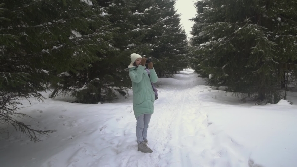 Beautiful Young Woman in Winter Clothing, Mittens and Wool Hat Photographing Snowy Forest
