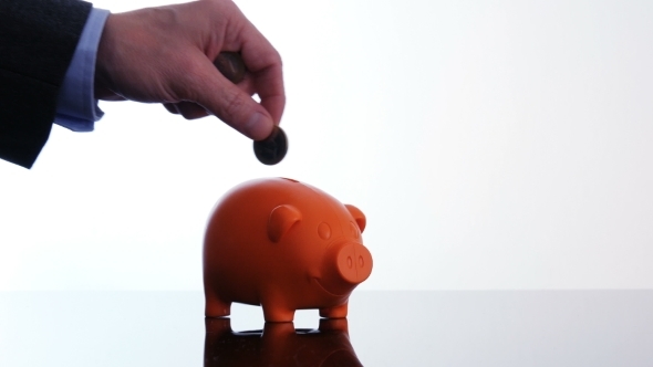 Male Hand Putting Coins in a Piggy Bank