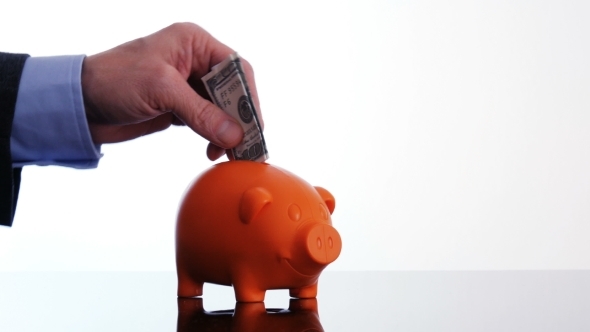 Male Hand Putting a Dollar Bill in a Piggy Bank