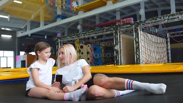Mother and Girl Using Phone in Gym for Watching Video How Do Jumping Exercise alt
