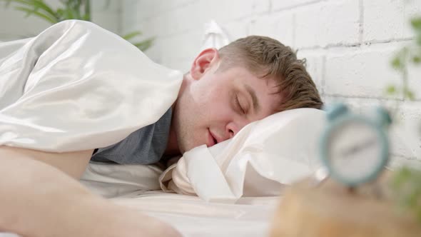 Man Sleeps in Bed with Clock in Foreground alt