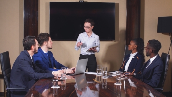 Female Manager Standing To Address Team at Business Meeting. alt