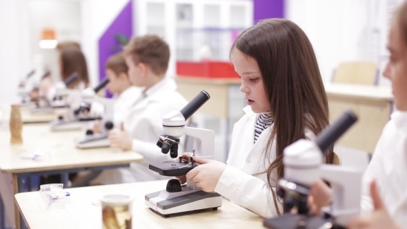 Little Girl Is Looking Through a Microscope at a Lesson in School