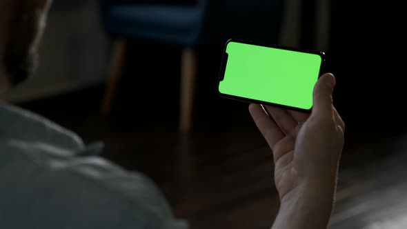 Man at Home Lying on a Couch using Smartphone with Green Mock-up Screen, Doing Swiping, Scrolling alt