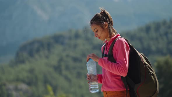 Woman Hiker is Thirsty and Drinks Water From a Plastic Bottle at During Hike in Mountains at Sunny alt